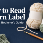 Cream and sage yarn skeins with blank paper bands, a crochet hook and measuring tape on a navy background, beside the title How to Read a Yarn Label.